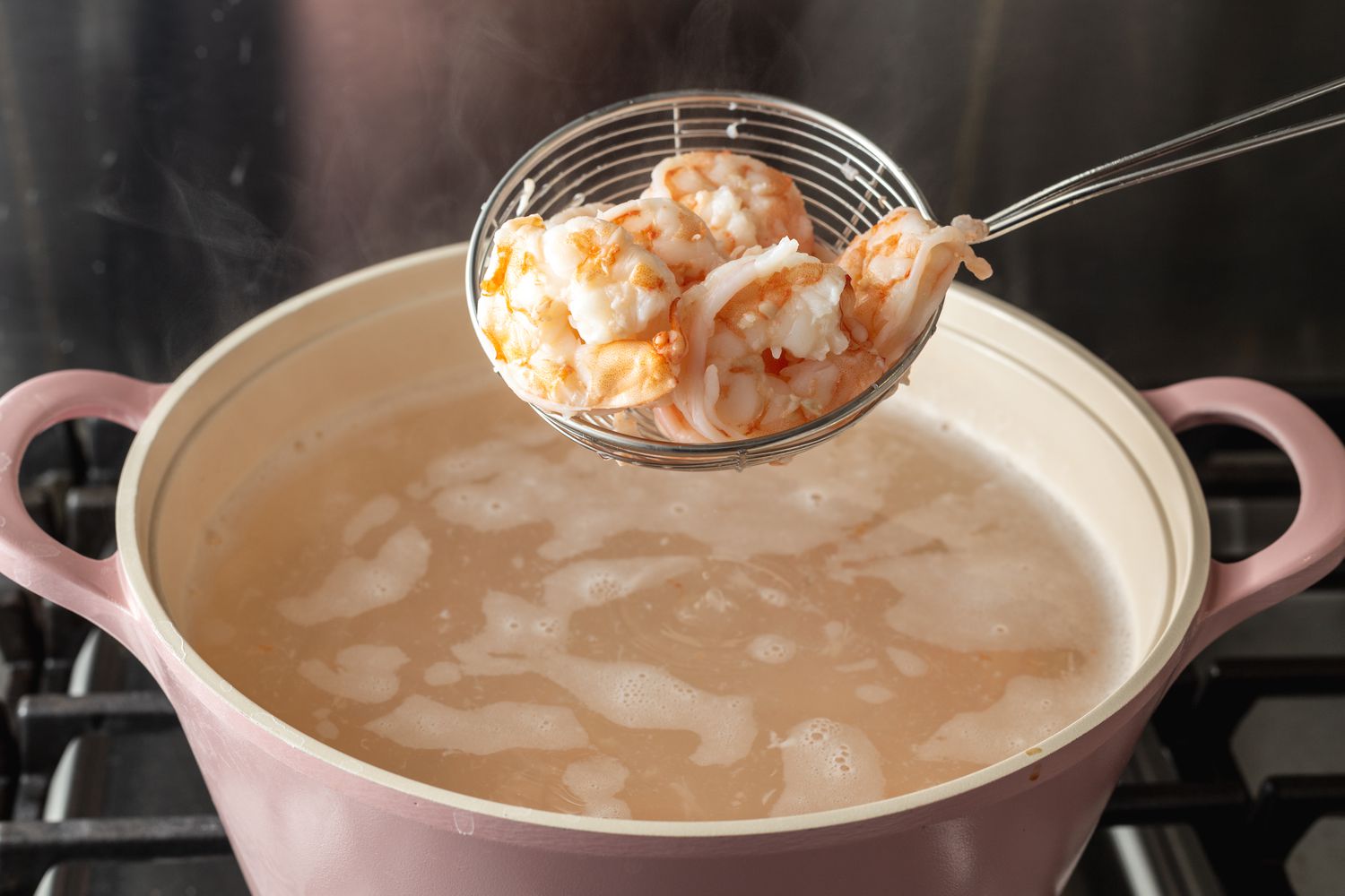 Spooning shrimp from a pot of water to show how to cook raw shrimp.