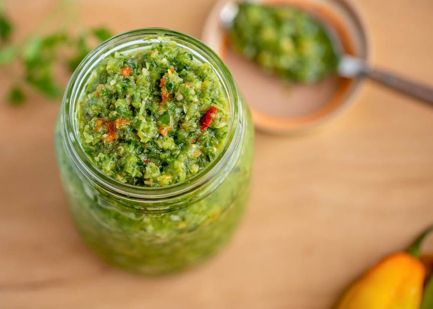 Overhead shot: jar of Carribbean green seasoning, and in the background (blurry), a spoon resting on the jar lid