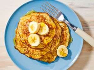 Overhead view of a blue plate of 2-ingredient pancakes topped with bananas next to a fork, all on a wooden tabletop