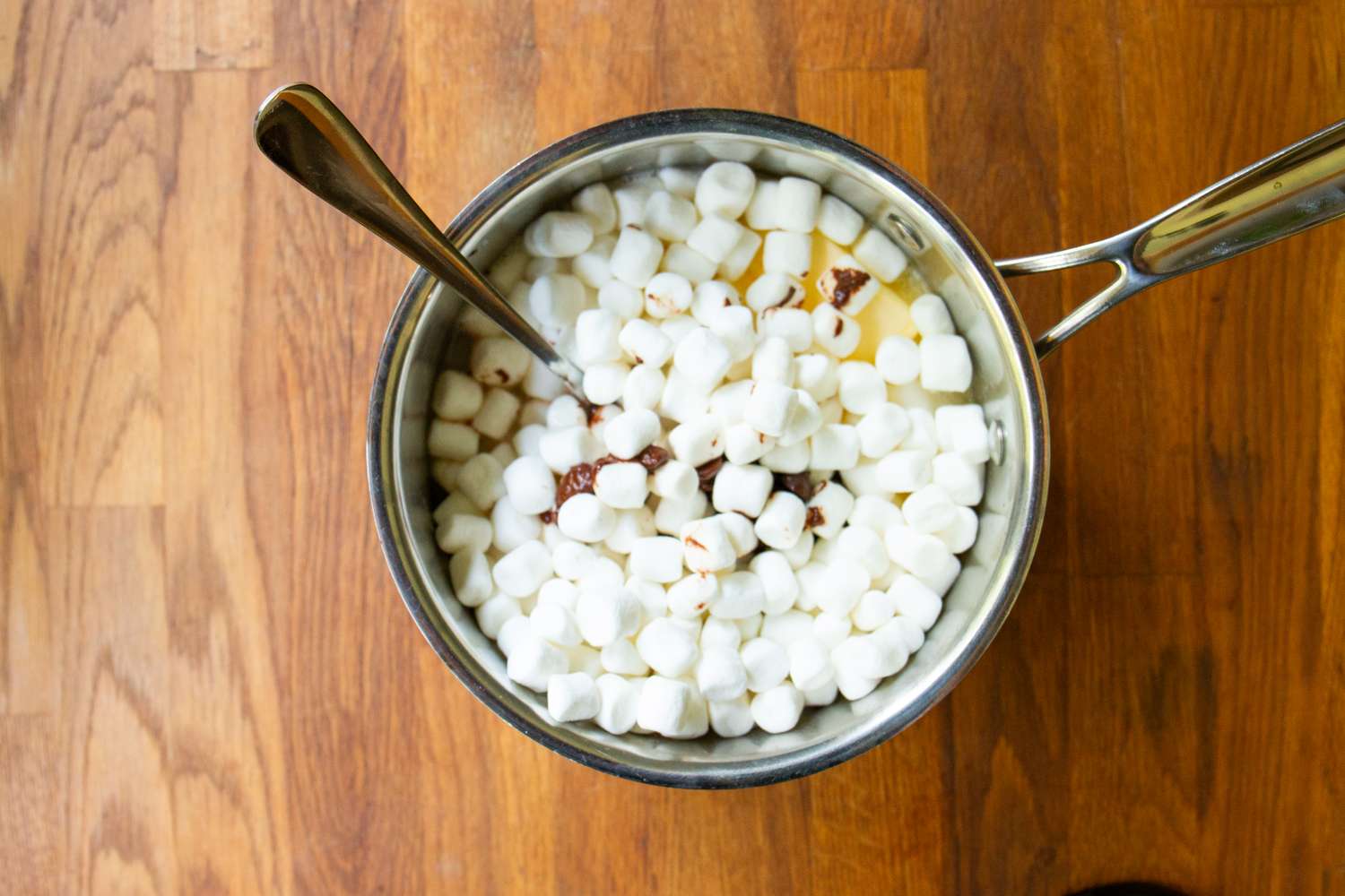 A saucepan containing marshmallows and melted ingredients on a wooden surface with a spoon inside