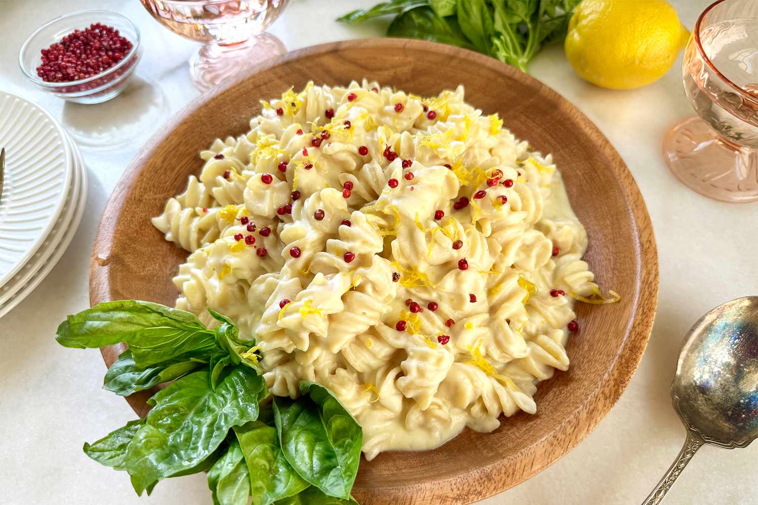 A dish of pasta topped with a creamy sauce garnished with lemon zest herbs and spices served on a wooden plate with basil leaves