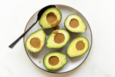 Halved avocados with dressing in their pits served on a plate with a spoon
