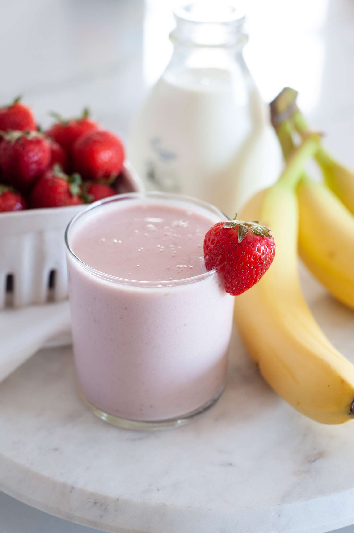 Smoothie with strawberry and bananas with a strawberry garnish and whole strawberries and bananas set around the cup.