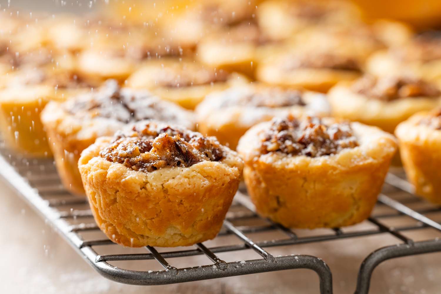 Powdered sugar sprinkled onto pecan pie cookies on a cooling rack