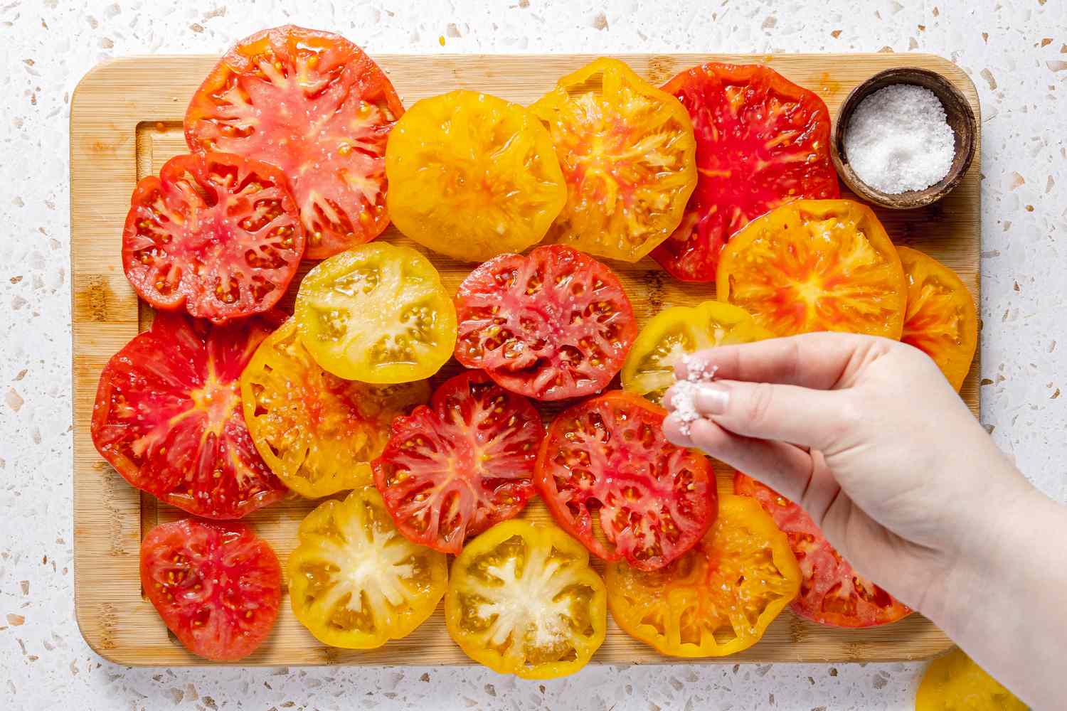 Salt Sprinkled Onto Heirloom Tomato Slices on a Cutting Board With a Small Bowl of More Salt for Caprese Salad With Tomatoes, Basil, and Mozzarella Recipe