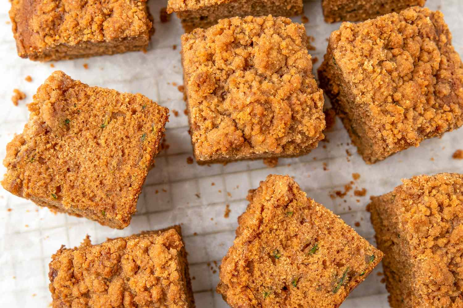Several pieces of zucchini coffee cake with a crumbly topping on a gridpatterned background