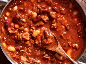 Pot of chili with beans and meat stirred with a wooden spoon