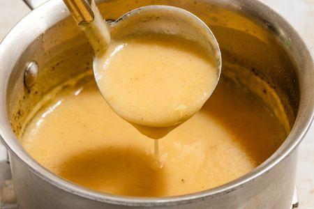 Angled view of a pot of gravy with a ladle removing a serving