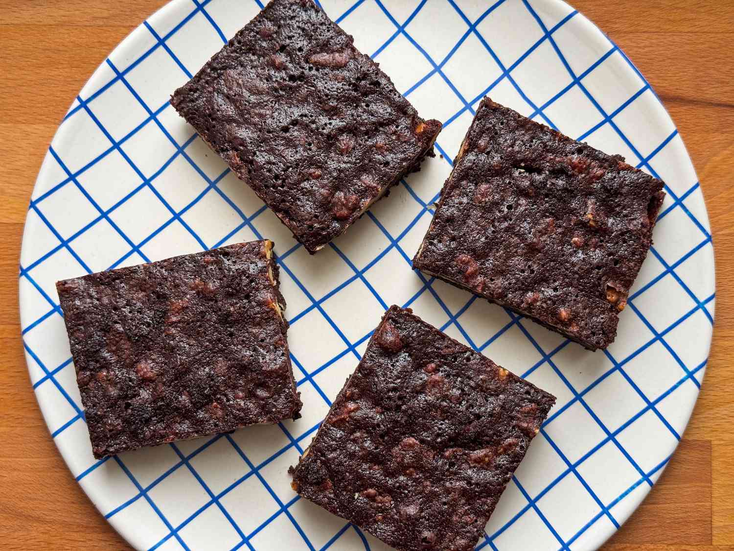 Four dark chocolate brownies on a white plate with a blue grid design