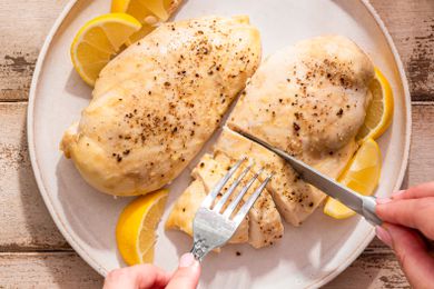 chicken breasts on a plate (one breast cut into pieces using a fork and knife) with lemons slices