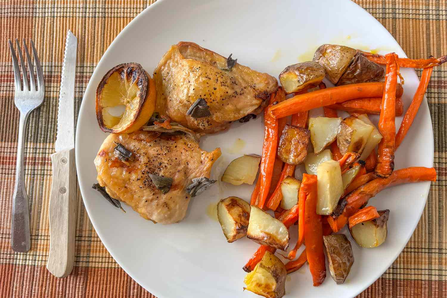OVerhead shot of a plate with two baked chicken thighs and a side of roasted carrots and potato