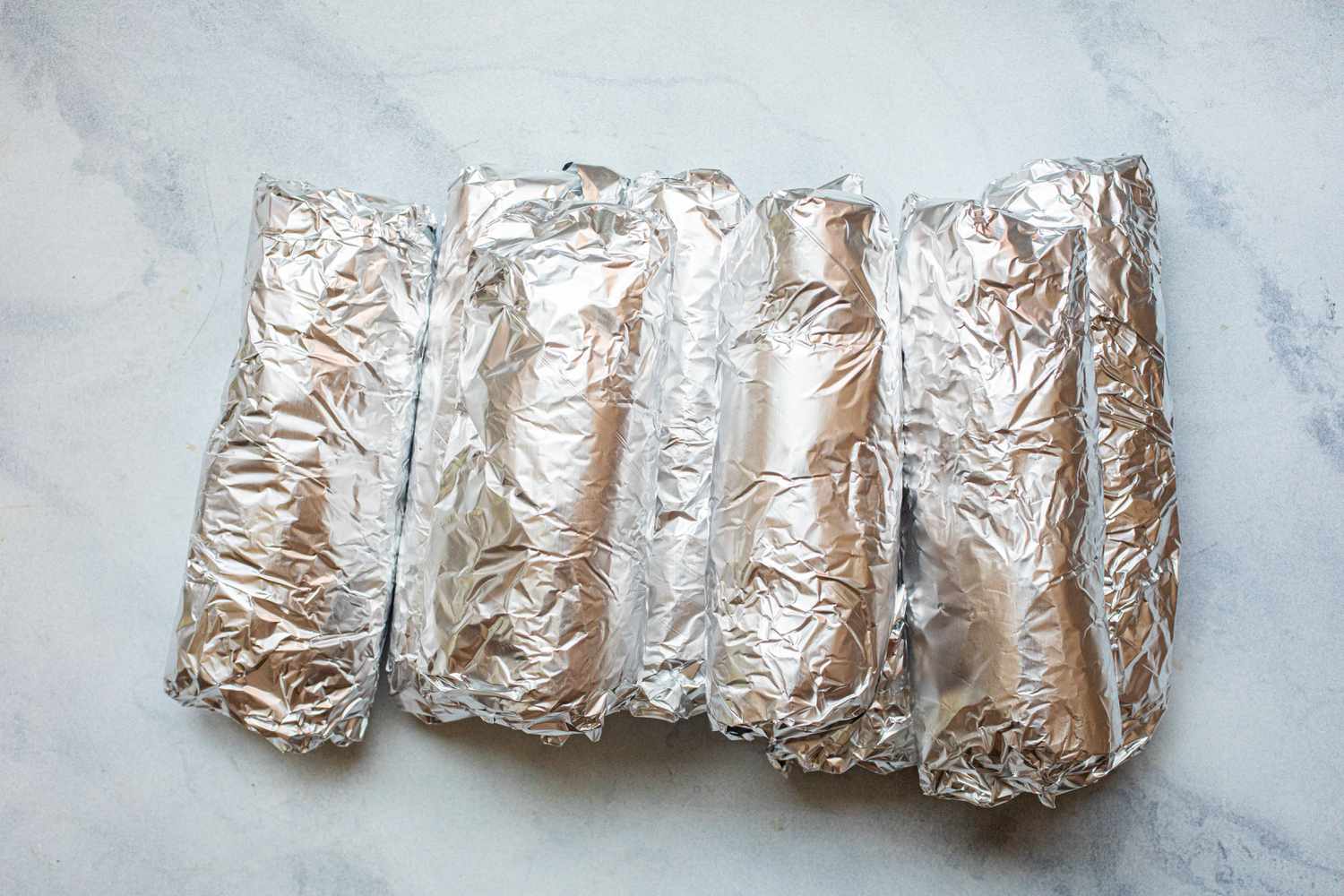 A row of Veggie burritos with beans, corn, and peppers wrapped in foil.
