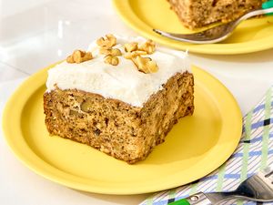 A slice of banana bread cake with frosting and walnuts on a yellow plate