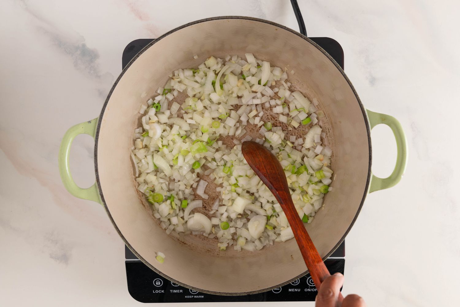 Aromatics sauteed in Dutch oven on a portable induction stove for Filipino beef stew recipe