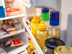 Condiments arranged on the inside door shelf of a refrigerator including mustard bottles and jars with other food items visible on shelves