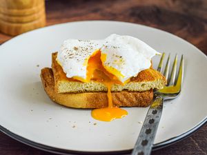 Side view of a poached egg on halved toast with the yolk running over the side.