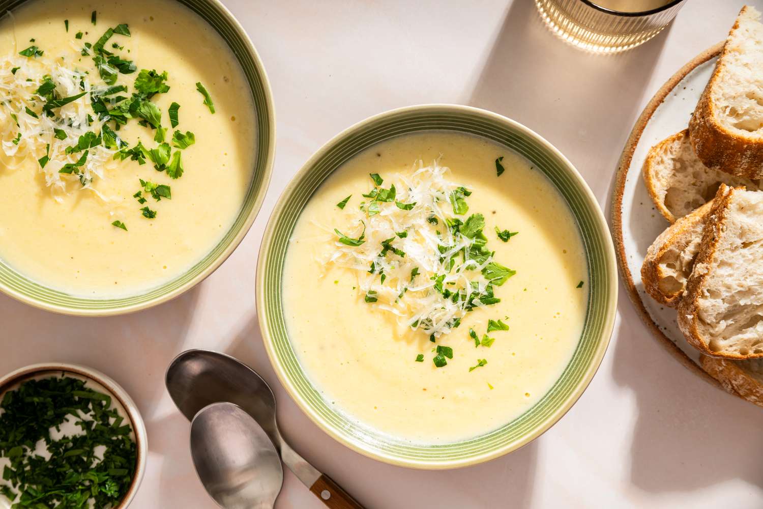 Two bowls of creamy potato soup garnished with herbs and accompanied by bread slices on a plate