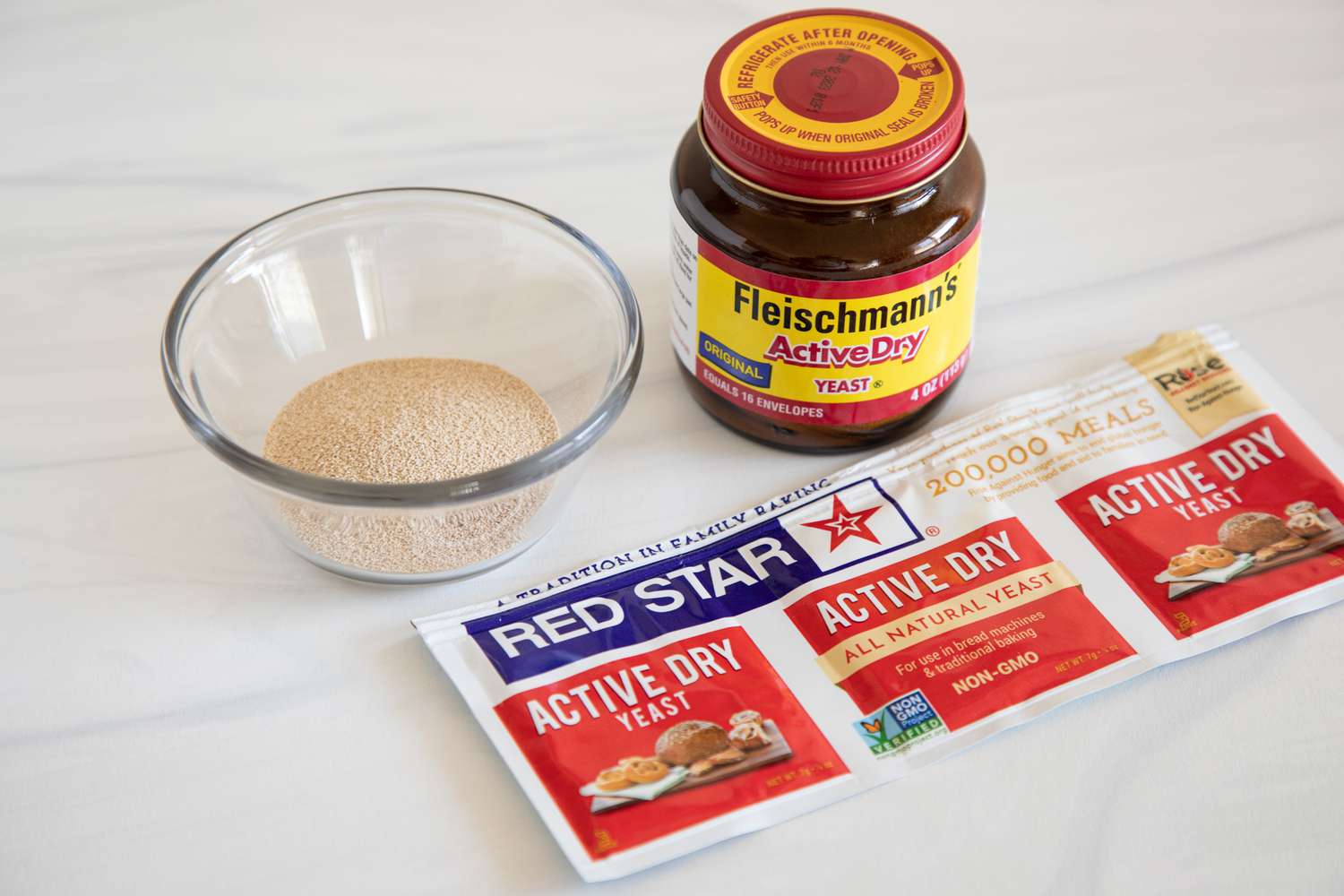 A jar of yeast, a glass bowl with yeast, and packages of yeast set next to each other for A Guide to Baking Yeast.