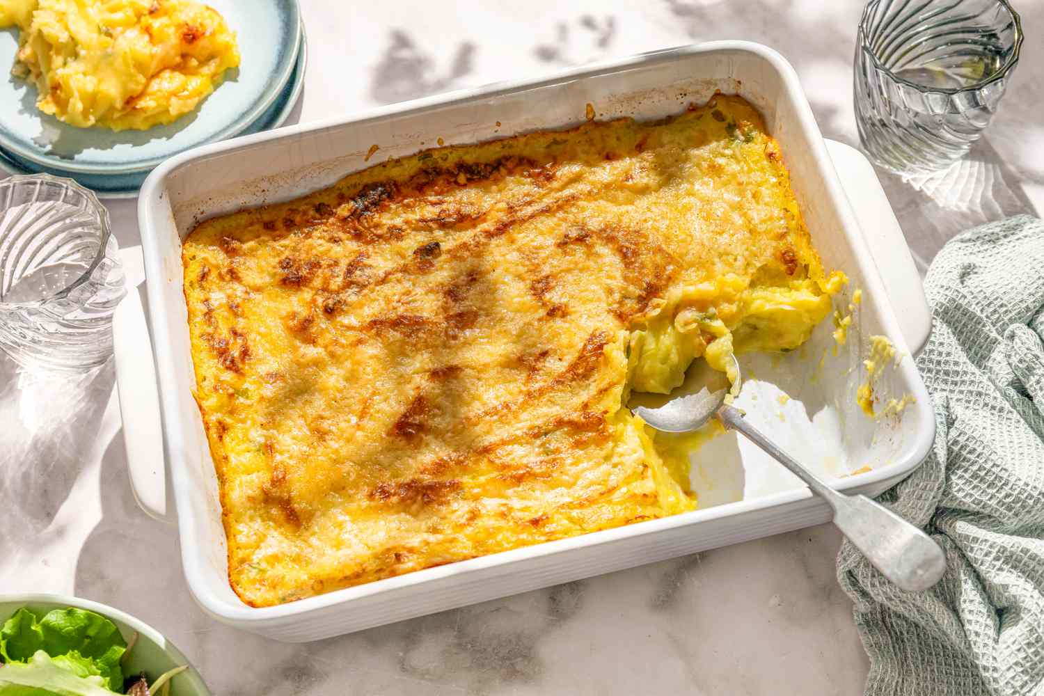 A white casserole dish with Irish baked mashed potatoes, with part of the dish scooped out, on a white marble counter
