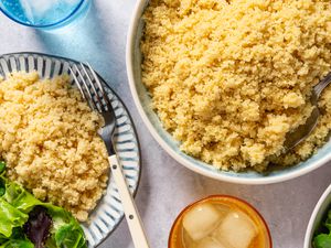 Overhead view of a large bowl of Cheesy Couscous with a serving spoon next to a serving plate with fork and lettuce