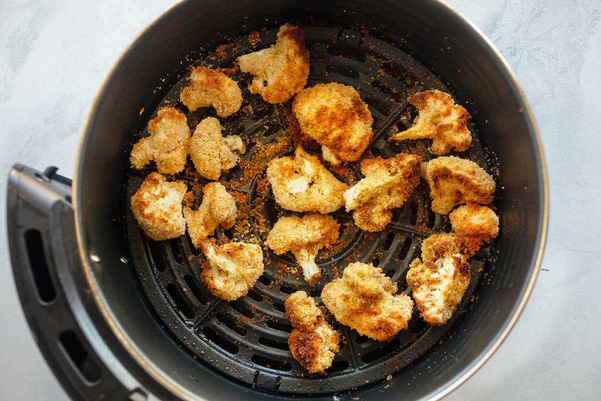 Golden air fried cauliflower florets inside a black air fryer.