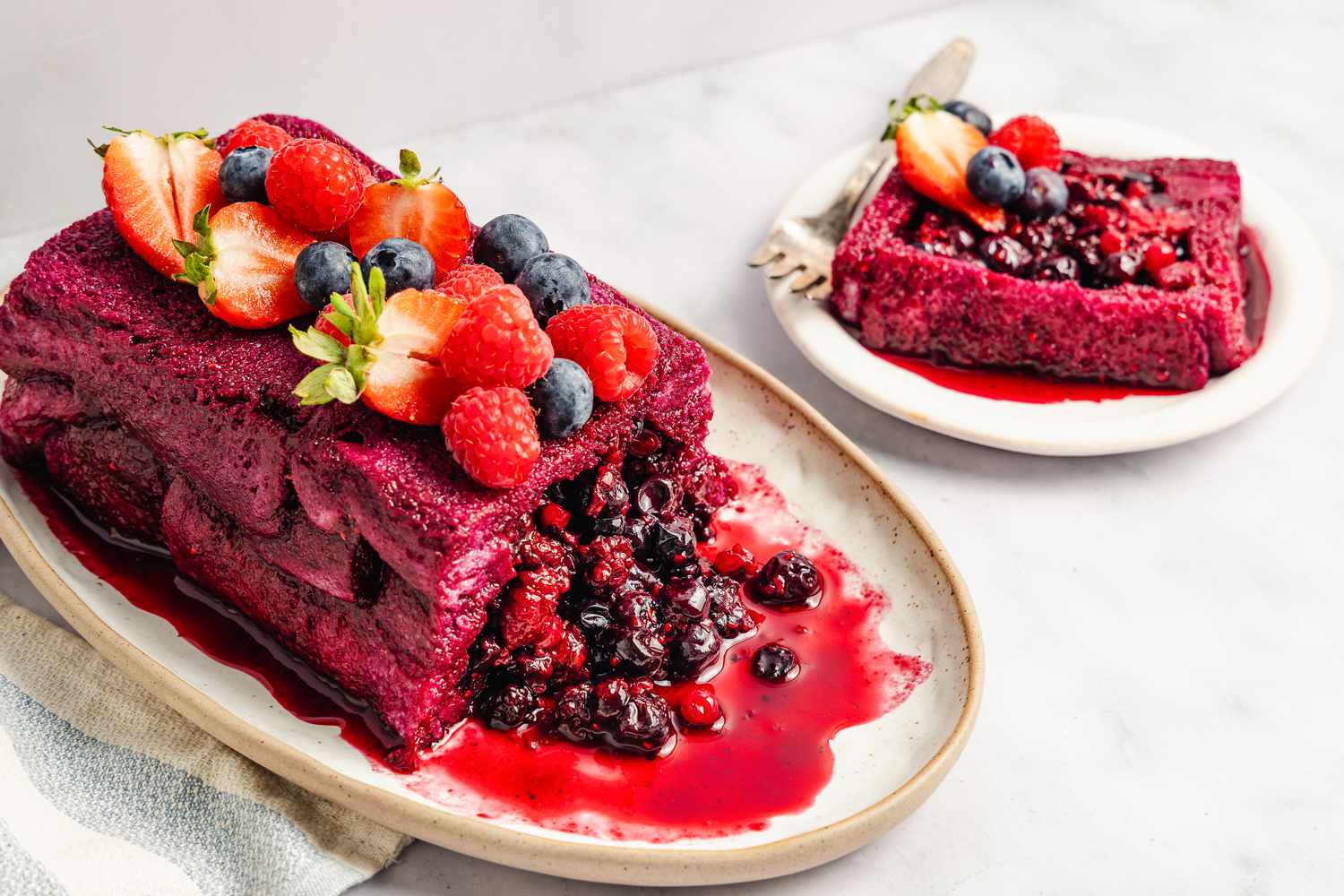 A summer pudding topped with fresh berries on a platter, adjacent to a single-serving slice on a plate
