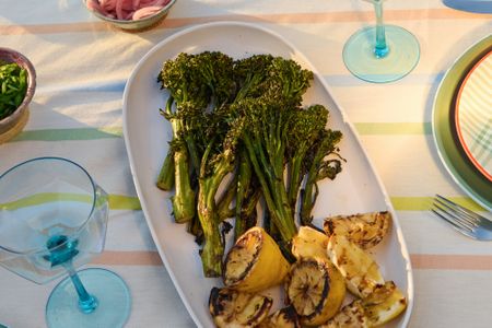 Platter of grilled broccolini and lemon slices on a table set with dishes and glasses