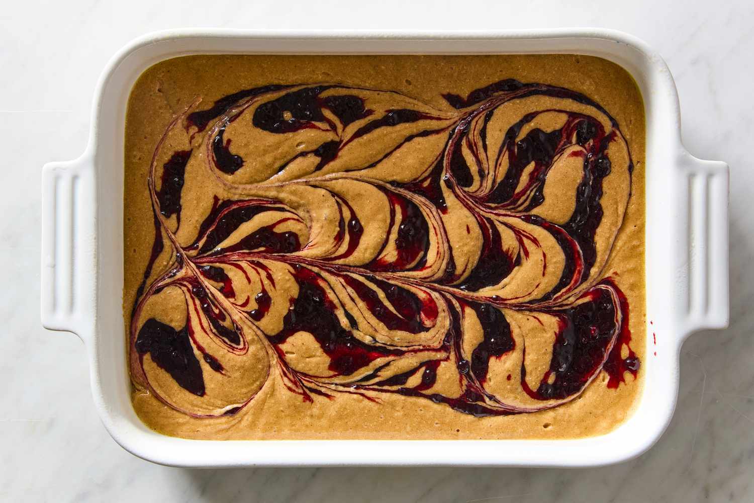 Jam beautifully swirled into the batter of the Easy Jam Cake recipe in a white balking dish