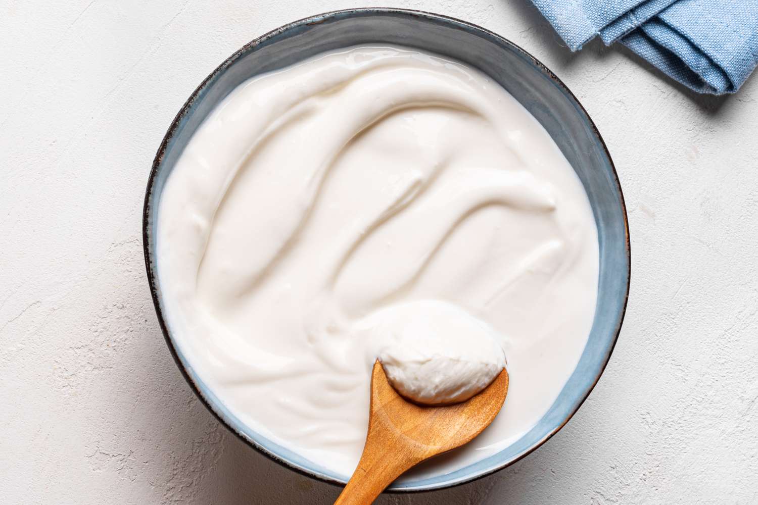 A bowl of creamy white yogurt with a wooden spoon resting inside it