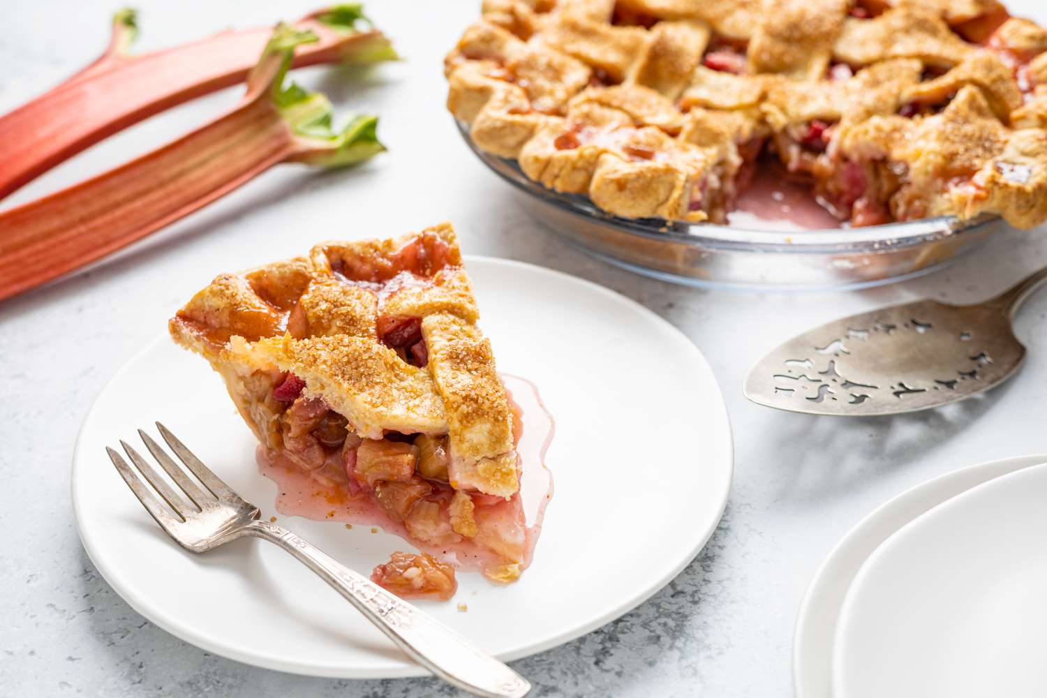 Slices of Rhubarb Pie on a Plate with a Fork Surrounded by Rhubarb and Pie Dish with More Pie