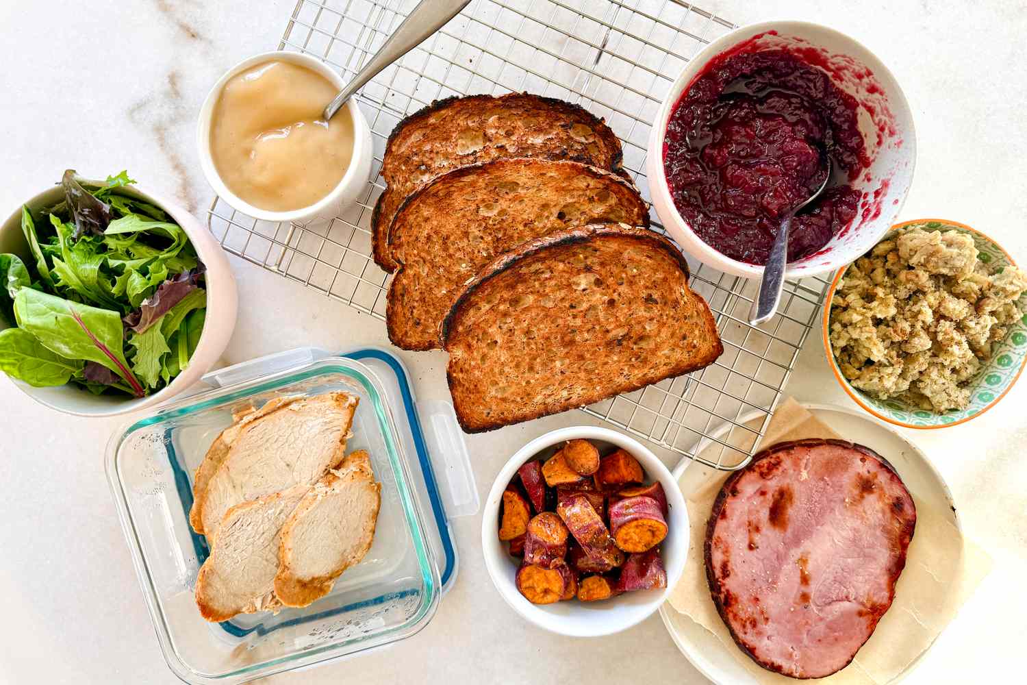 Ingredients for making sandwiches including bread turkey slices ham mixed greens cranberry sauce gravy stuffing and roasted vegetables