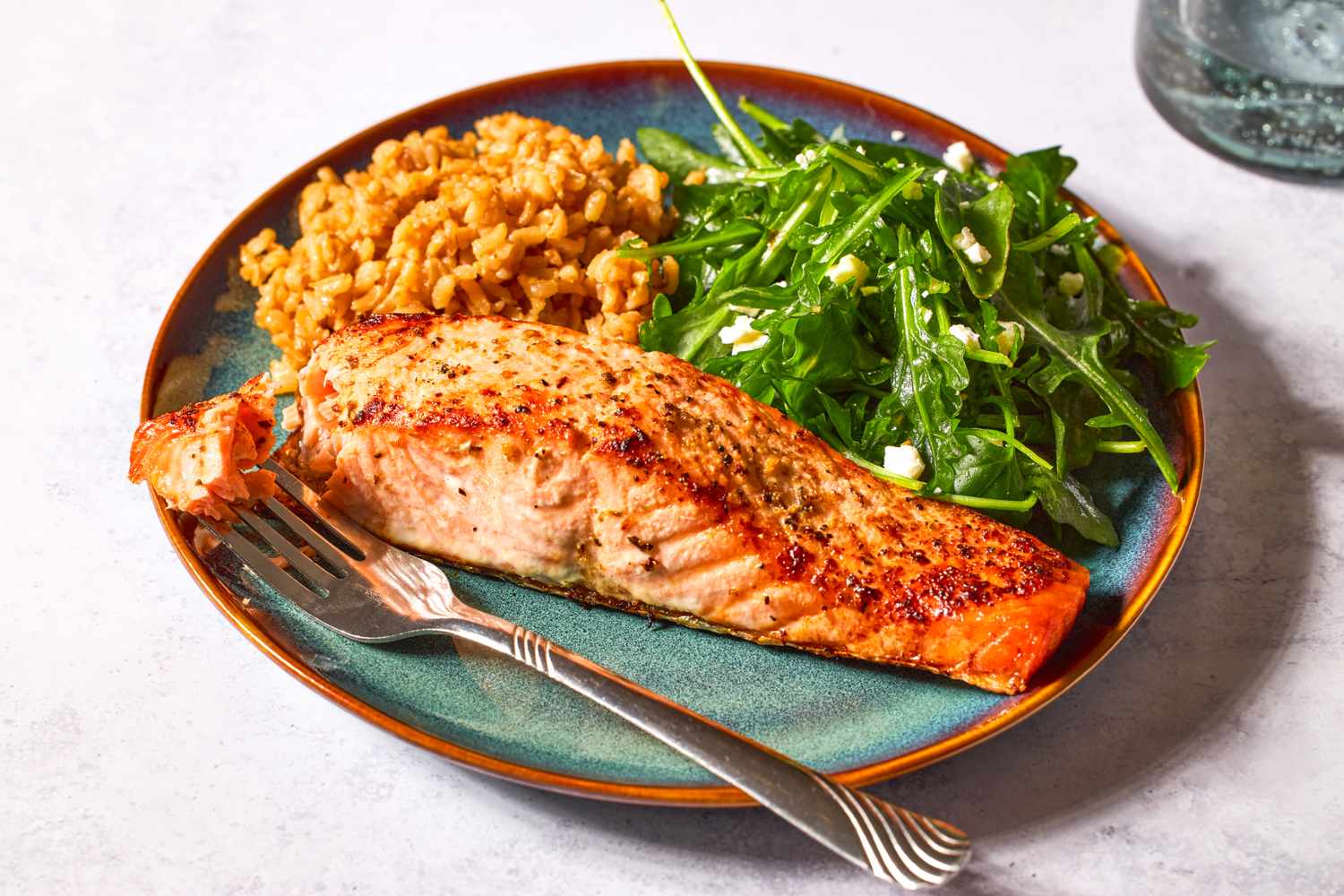 Cooked salmon served on a plate with greens and a grain side dish