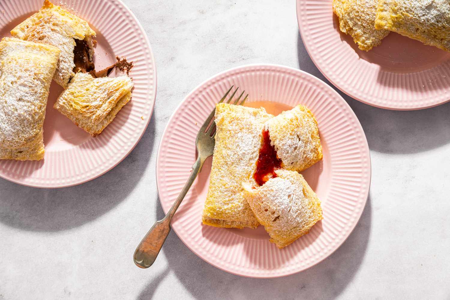 Toast Pies on pretty pink dessert plates, one with a fork and one pie torn open to reveal red filling, another pie torn open to reveal brown filling