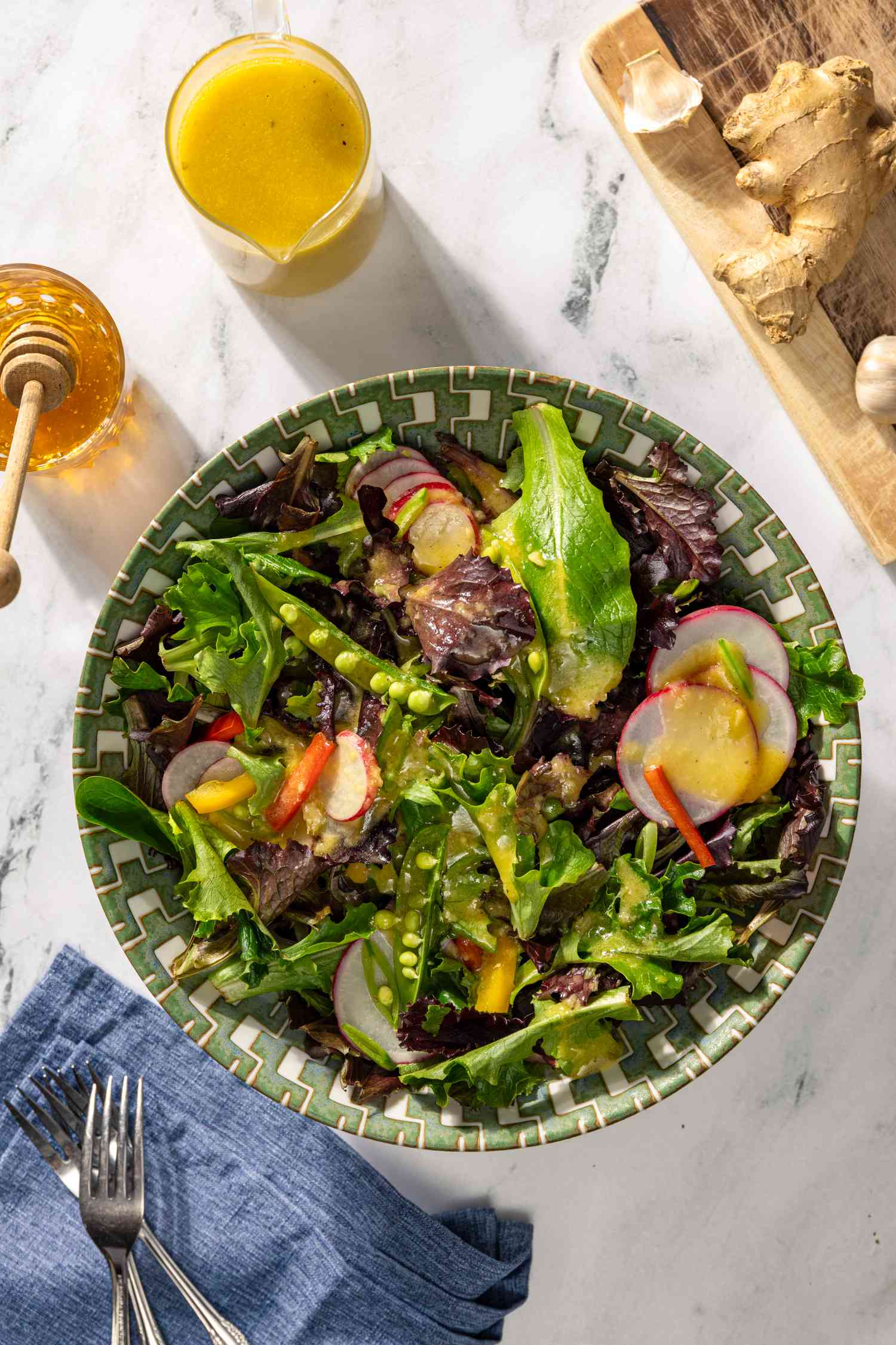 overhead view: ginger dressing on a mixed green salad at a table setting with a small container with more dressing and dressing ingredients