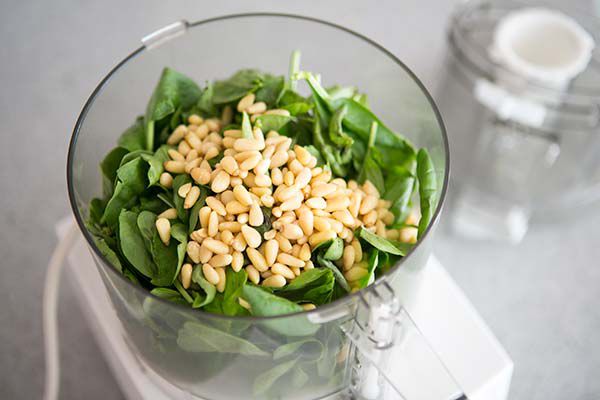 Basil leaves and pine nuts resting in a food processor 