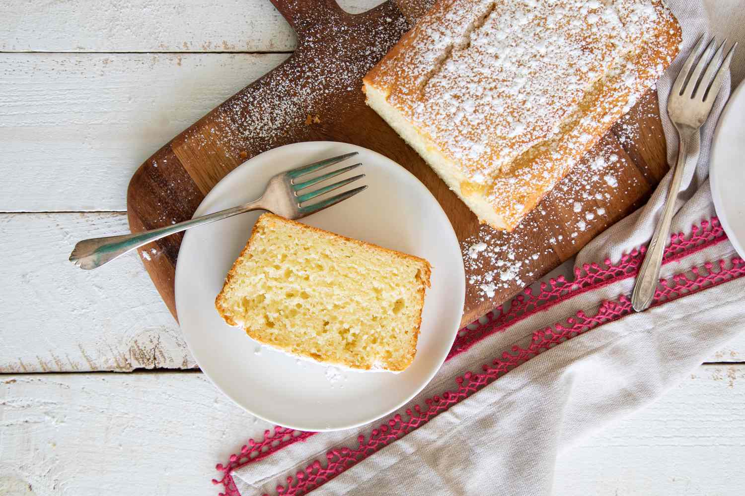 A slice of Olive Oil Yogurt Cake on a plate with the rest of the loaf next to it.