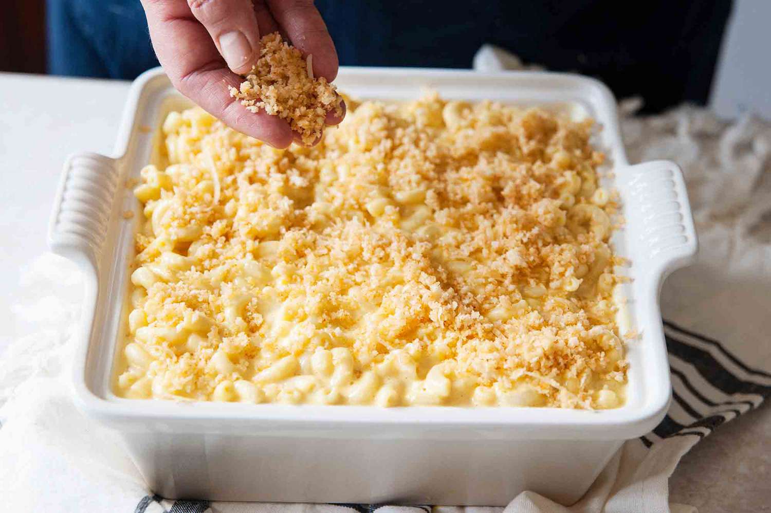 Best mac and cheese recipe -- hand sprinkling breadcrumbs ontop mac and chees in a white casserole dish