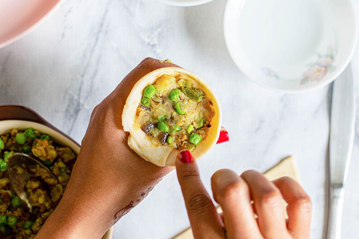Woman holding a cone of dough filled with vegetables in her hands ot make Indian Samosas.