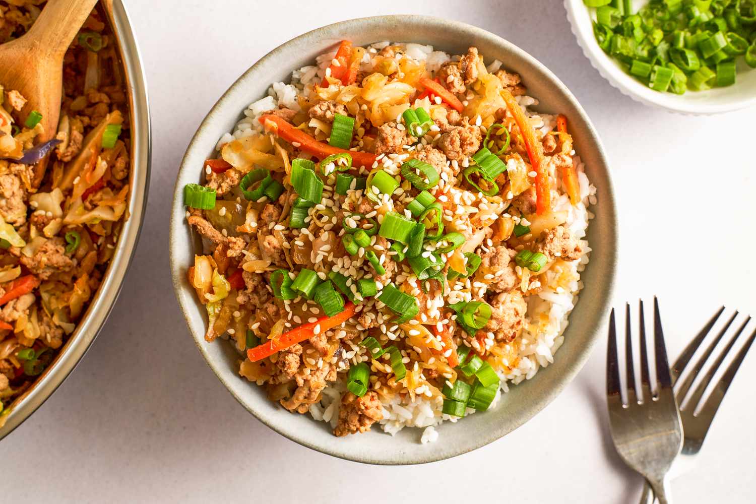 Overhead view of a bowl of egg roll in a bowl next to two forks and bowl of sliced green onions