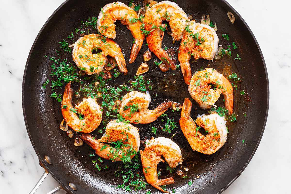 Large shrimp cooking in a non-stick skillet and covered with herbs.