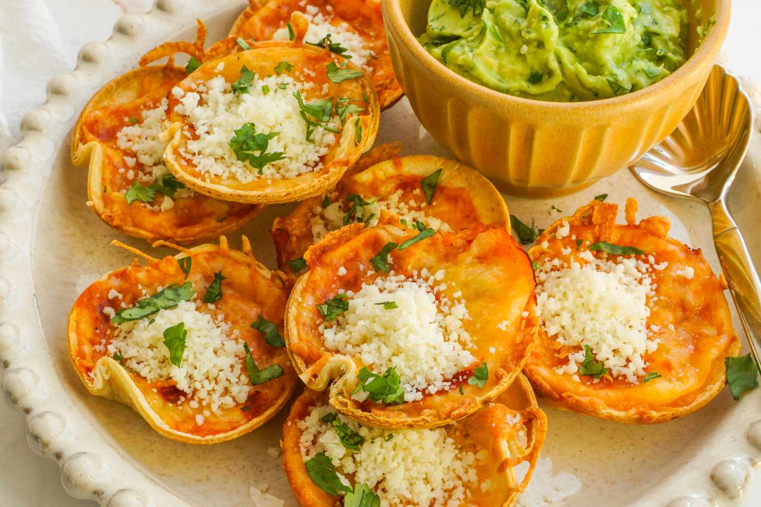 Platter of enchilada bites topped with cheese and herbs next to a bowl of guacamole