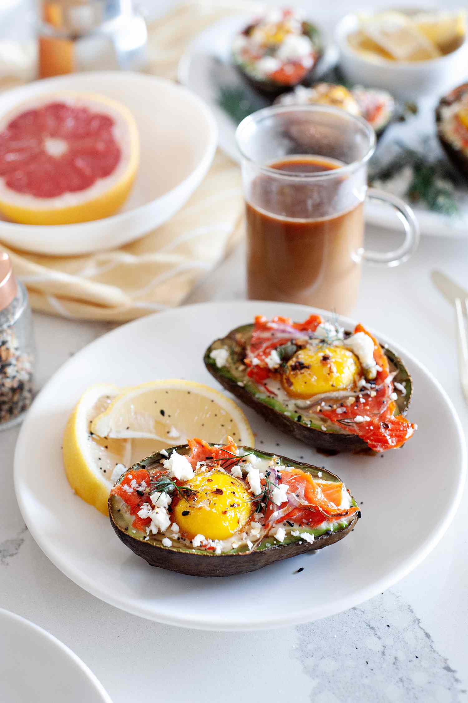 Baked eggs in an avocado on a plate with a lemon. Sliced grapefruit and drinks are behind it.