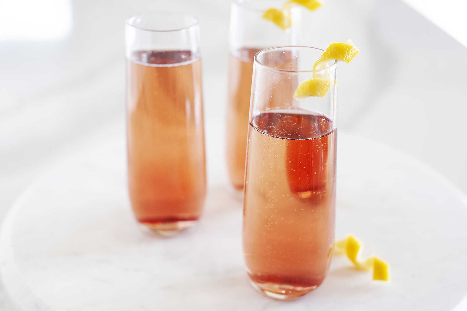 Side view of kir royale in three tall and slender glasses on a white background