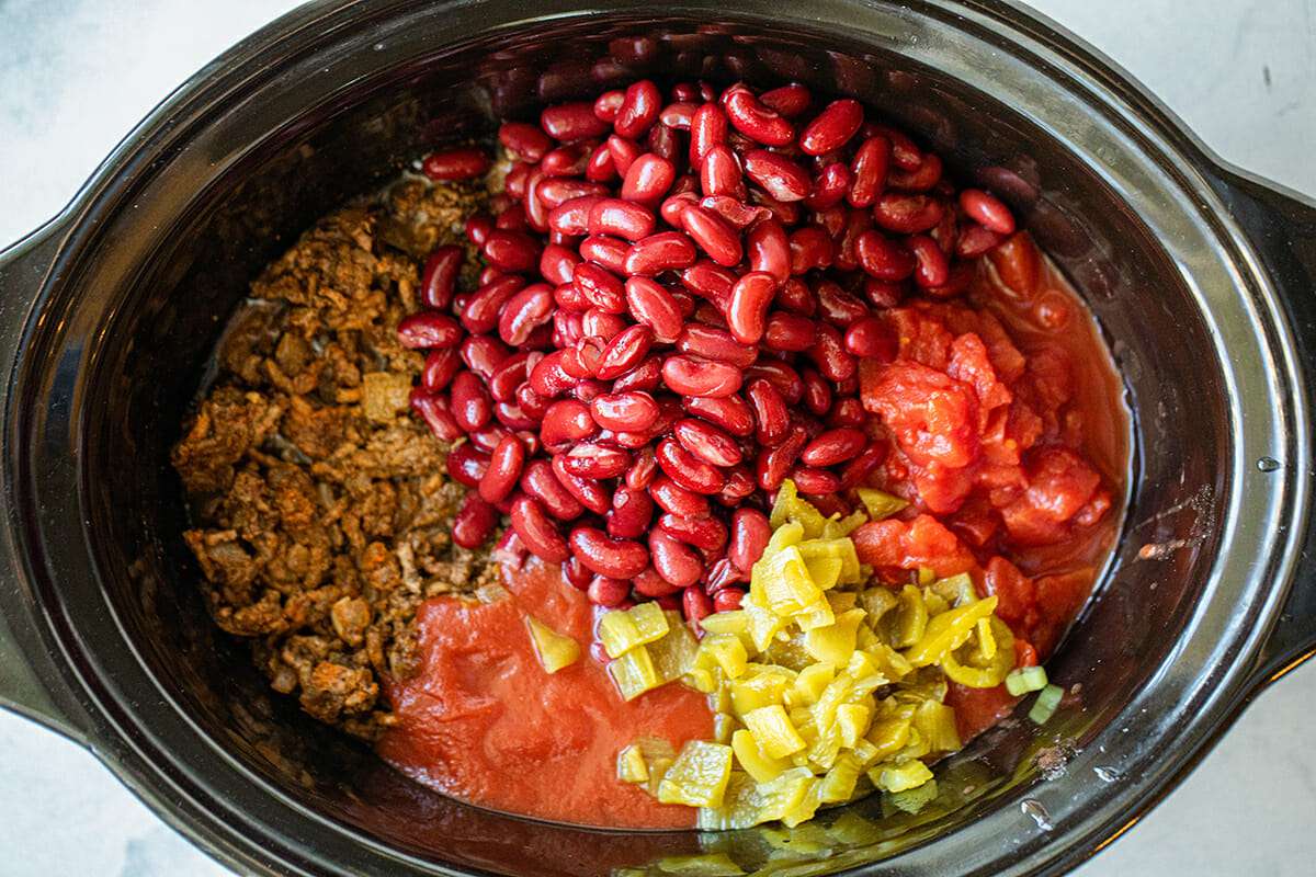 The Ultimate Slow Cooker Chili with beef, beans, green chilis and tomatoes placed around the inside of the crock pot.