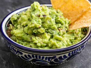 A bowl of guacamole with two tortilla chips i nit