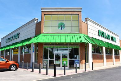 Entrance of a Dollar Tree store with visible signage and green awning parked orange car to the left