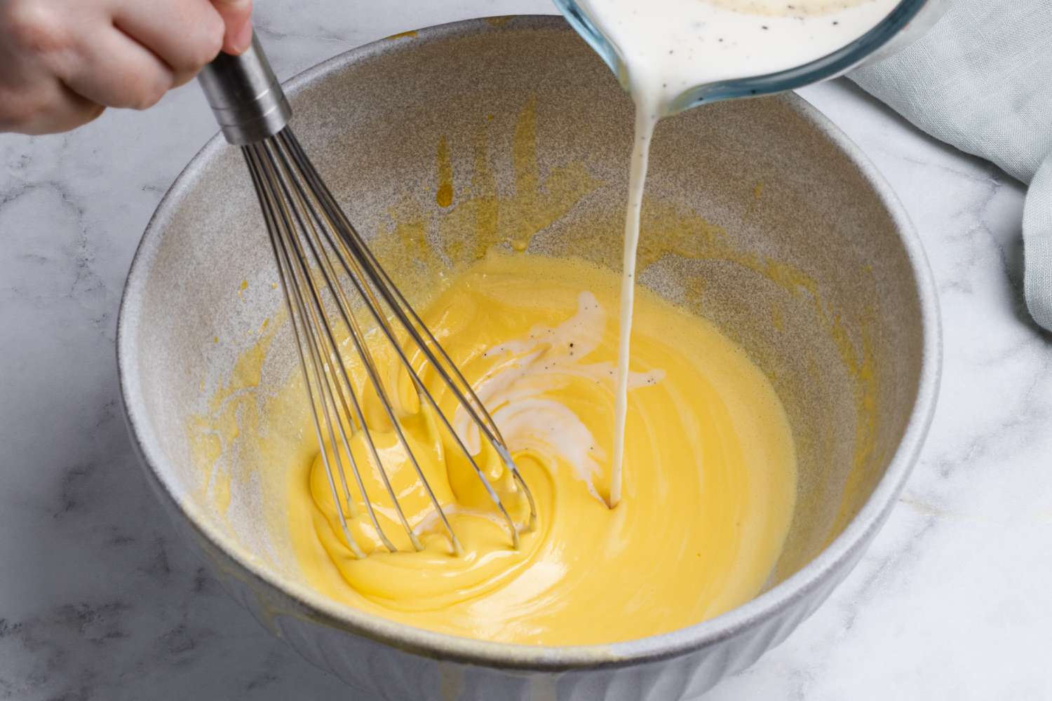 Adding custard to egg mixture for a homemade ice cream recipe.