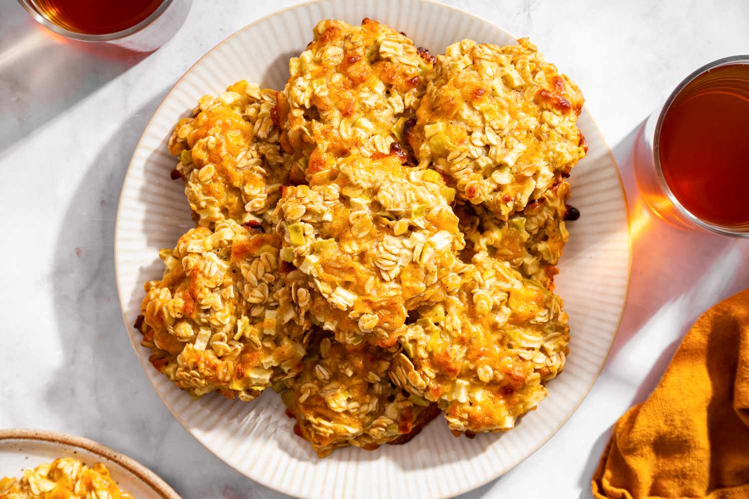 A plate of apple cheddar oat cookies surrounded by glasses of a beverage on a table