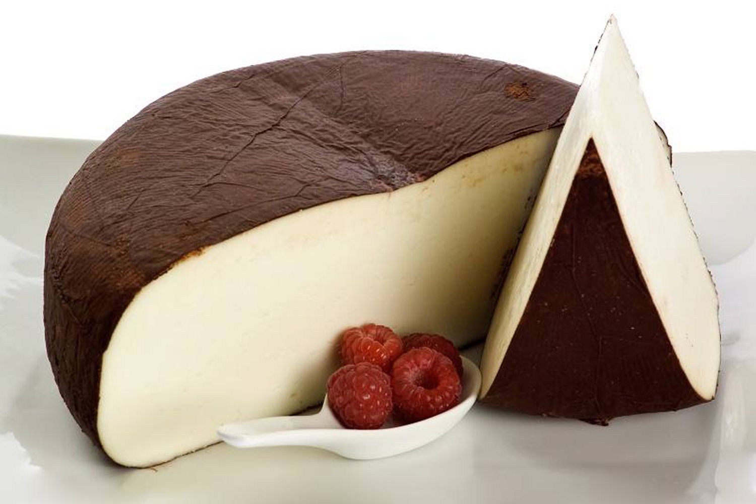 A wheel of Carr Valley Cocoa Cardona cheese cut in half with another thich slice of cheese and a spoon of raspberries in front