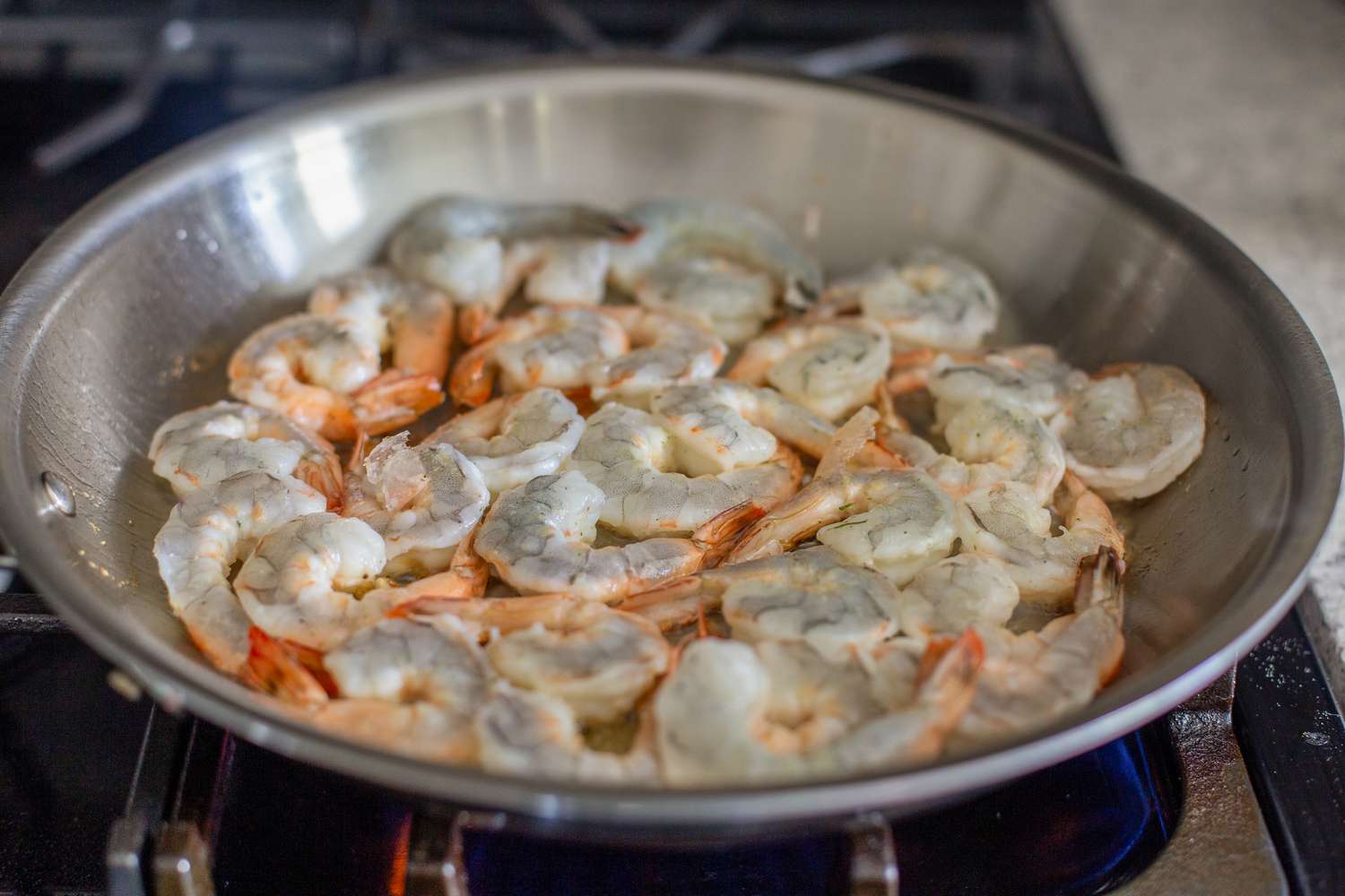 Shrimp in the Stainless Steel Pan on the Stove for 5-Ingredient Shrimp Pesto With Cherry Tomatoes Recipe. Shrimp Facing Pan Is Pink.